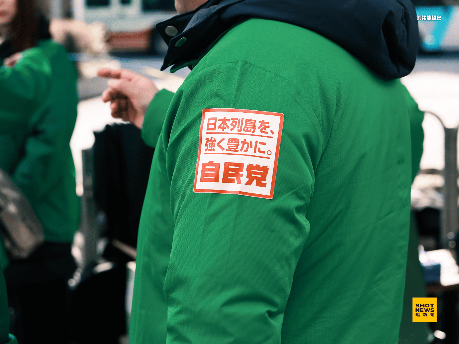 日本自民黨工作人員在選舉活動現場都會貼上「讓日本列島更加強大富裕」的臂章貼紙做識別與宣傳。(劉祐龍攝影)