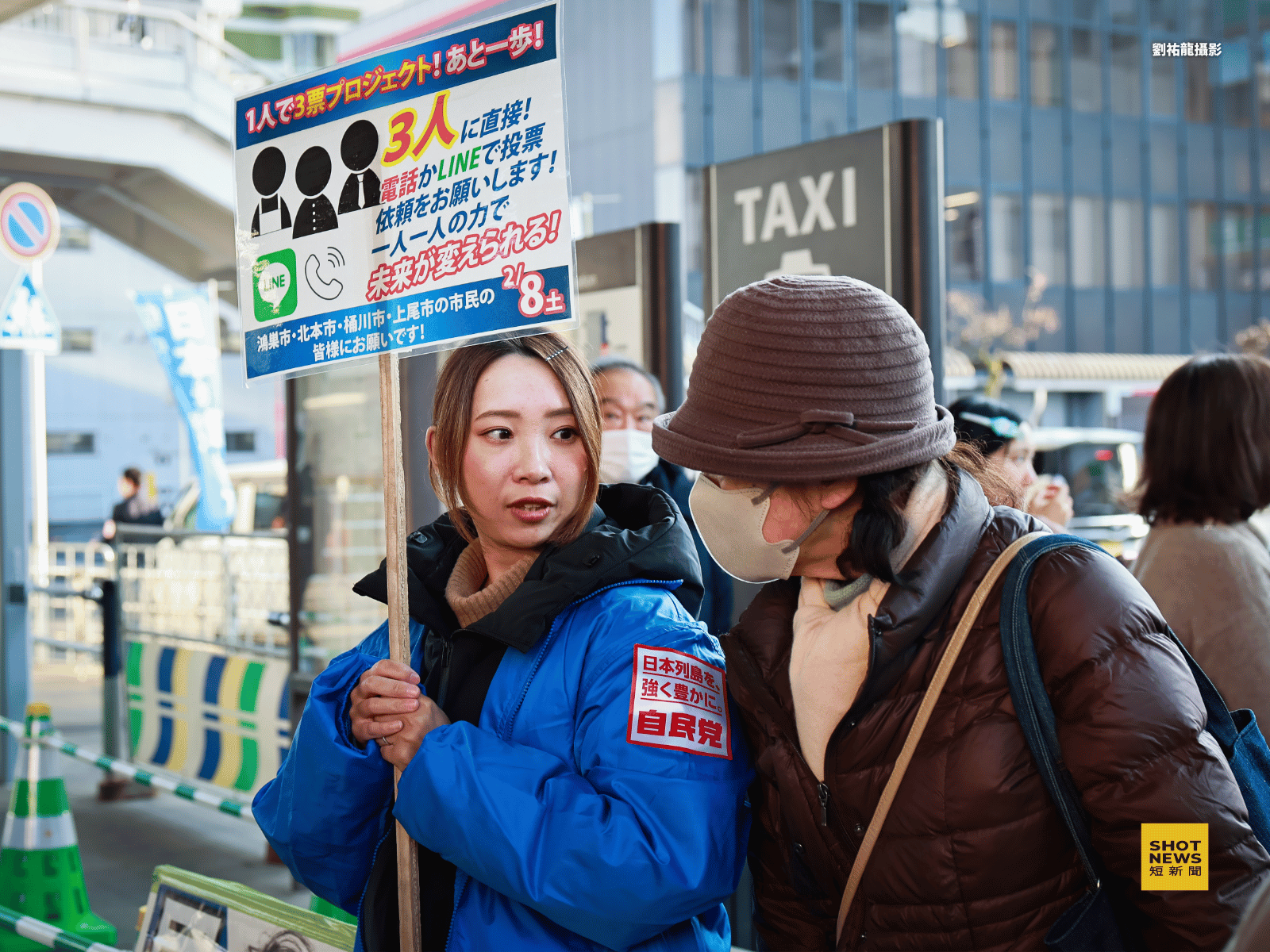自民黨工作人員高舉著「1人拉3票專案!還差最後一步!請透過電話或 LINE 請求對方投下一票!靠每個人的力量,是可以改變未來的!」的舉牌內容,除了傳統演講活動,也積極利用社群擴展選票與支持。(劉祐龍攝影)